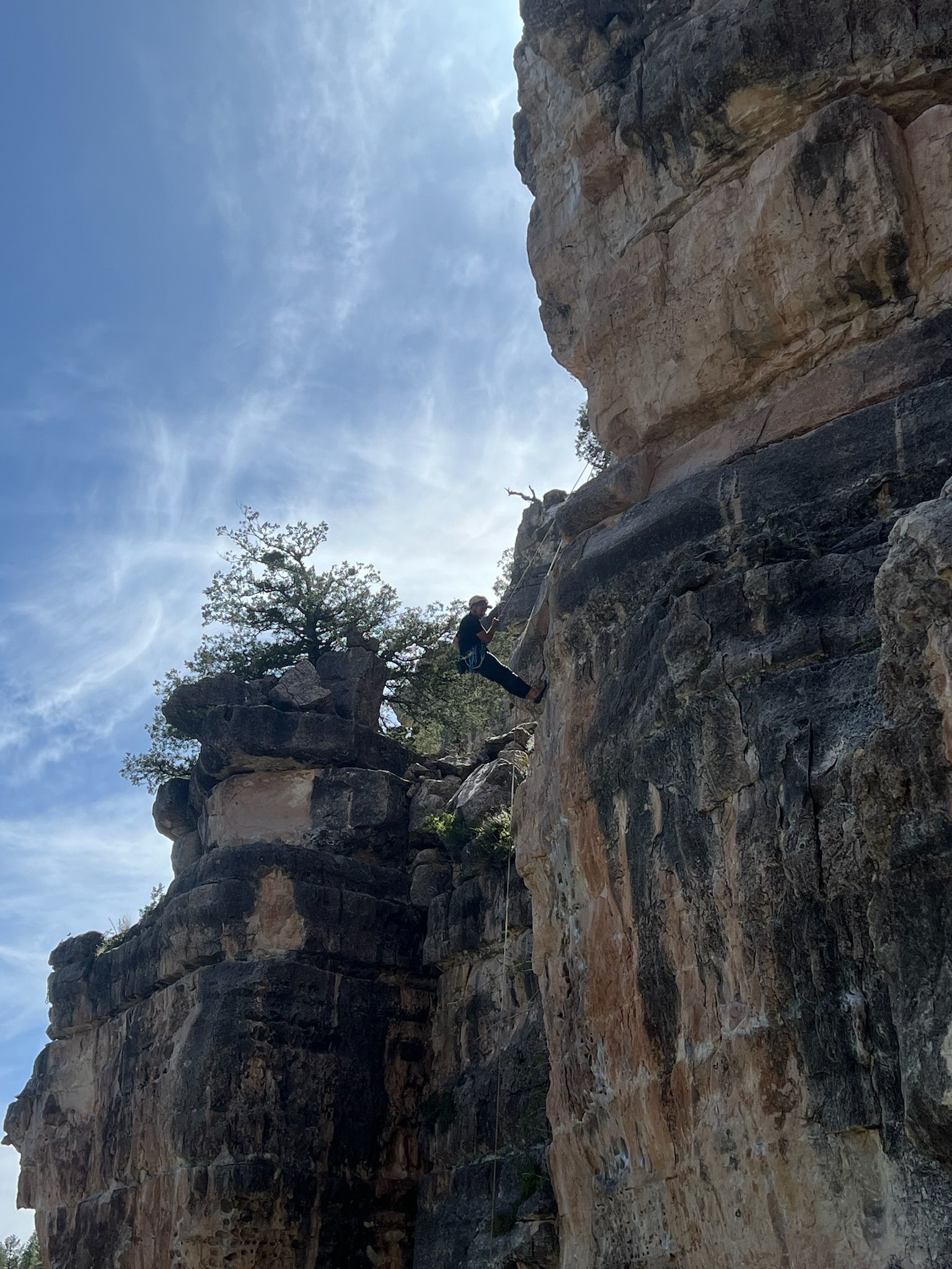 Man rappels from the top of a rock outside.